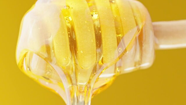 Healthy organic honey. Honey dripping from wooden honey spoon at yellow background. World bee and honey day. Close-up in 4K, UHD