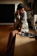 Woman, thinking and relax on kitchen counter in home for morning break, sitting and daydreaming on...