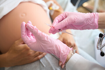 Cropped of doctor preparing syringe for injection in pregnant belly of patient