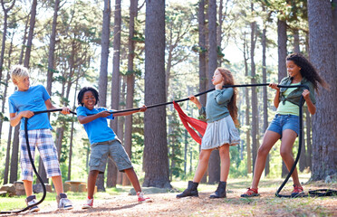Kids, rope and tug of war for play adventure, challenge and strength game in woods with summer camping. Children, diversity and competitive in forest environment and teamwork in power match by trees - obrazy, fototapety, plakaty
