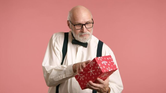 In a moment of pleasant surprise, a man in formal attire with suspenders opens a red gift box, curious if the Christmas presents are his. Camera 8K RAW.