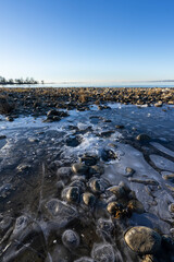 frozen puddle with stones on the shore of a lake in clear weather