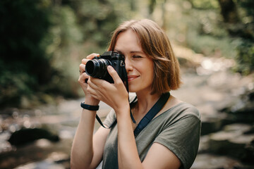 Young female traveler using camera while photographing the scenic view by the mountain river