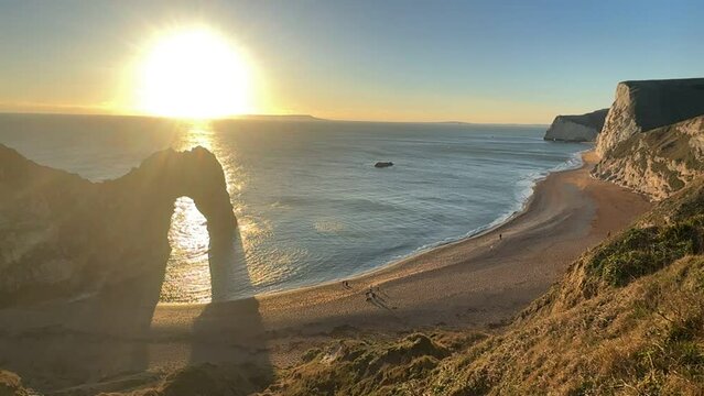 The sun goes down on the Jurassic coast and Durdle Door in Dorset with Seak Pink Trift growing on the top of the cliff in the foreground. Durdle Door, Dorset, Jurassic Coast, England, UK