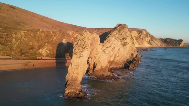 The sun goes down on the Jurassic coast and Durdle Door in Dorset with Seak Pink Trift growing on the top of the cliff in the foreground. Durdle Door, Dorset, Jurassic Coast, England, UK