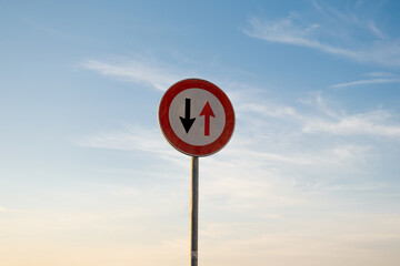 Give way to oncoming vehicles traffic sign, isolated sunset sky.