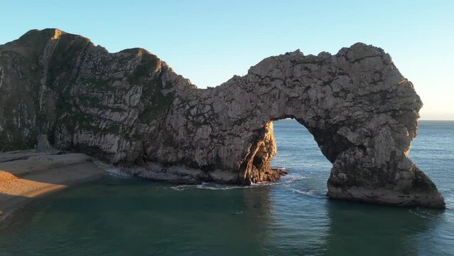 The sun goes down on the Jurassic coast and Durdle Door in Dorset with Seak Pink Trift growing on the top of the cliff in the foreground. Durdle Door, Dorset, Jurassic Coast, England, UK