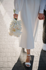 The bride and groom with a wedding bouquet, holding hands and walking on the road on the street. Outdoors. Down view.