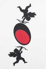 two traditional machine-cut black paper cupids with bows and arrows on white paper with red on...