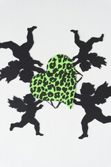 black paper silhouettes of machine-cut winged figures (Cupids) with bows and arrows arranged around a green heart with spots 