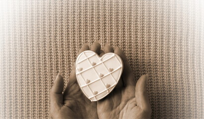 A close-up view of a person holding a white, heart-shaped cookie on a pink knitted surface,...