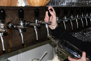 Behind the counter. Women's hands beautifully and easily pour beer into a bottle.
