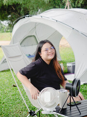 Happy Asian woman sitting on camping chair rest on vacation with tent in natural park