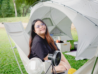 Happy Asian woman sitting on camping chair rest on vacation with tent in natural park