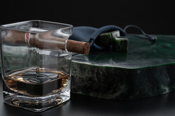 Still life of a glass of whiskey with jade stones for cooling and a cigar