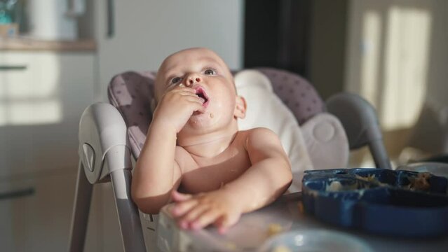 baby dirty eats. happy family a child toddler concept. baby dirty sitting messing with food at the table for feeding in the kitchen. grimy toddler lifestyle in the kitchen