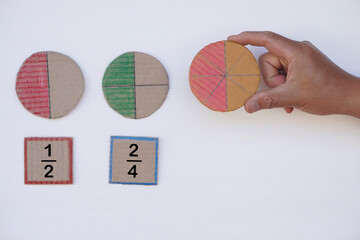 Math teaching materials about fraction. Hand holds circle paper to show parts of color separation. Concept, education. DIY craft as teaching aid in Math subject.        