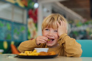 happy boy with blond hair eats fries and nuggets in restaurant