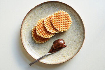 Round waffle cookies and chocolate cream on a plate with a white background
