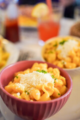 Creamy mac and cheese in a pink bowl, garnished with herbs.