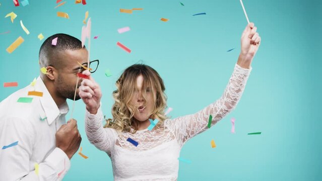 Confetti, dance and happy couple in studio for celebration, success and winning competition or valentines day party. Funny man and woman or young people with costume glasses on a blue background