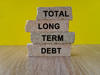 Total long term debt concept with words on brick blocks. Beautiful wooden table, yellow background....