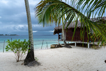 Red beach hut on San Blas island behind palm tree leaf and white sand beach