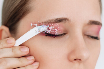 Cropped shot of a young caucasian woman with her eyes closed applying purple and pink eye shadow...