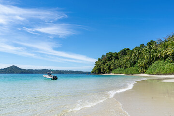 Beautiful white sand and blue sea with single boat to the left and jungle to the right on tropical island