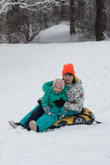 mom and daughter are riding a snow slide in the forest. Snow-white winter