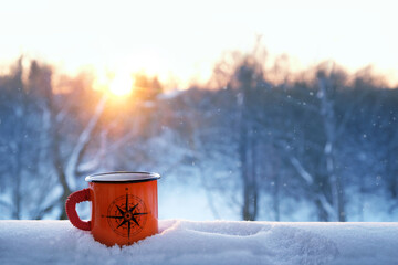 orange enameled traveler tea mug with image of compass wind rose close up in snow outdoor. winter...