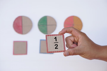 Hand hold paper card with fraction numbers. Circle paper show parts of color separation. Concept, Math teaching. Education. DIY craft as teaching aid in Math subject.                  