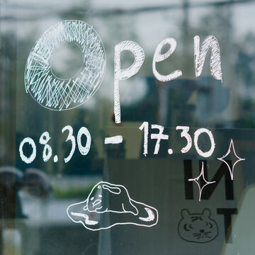 Handwritten opening time message on coffee shop window.