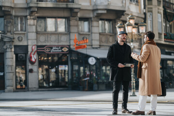 Two fashionable men talk on a city street, exuding urban lifestyle and casual business interaction against a backdrop of shops.