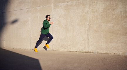 Adult athletic man running fast along concrete wall in the city