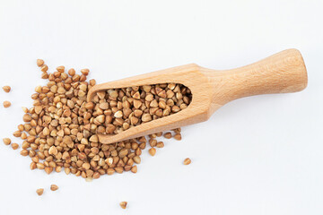 Wooden scoop of roasted buckwheat on a white background.