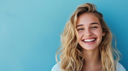 Photo with space for text. Portrait of a blonde girl with a smile and white teeth on a blue matte background. Suitable for advertising