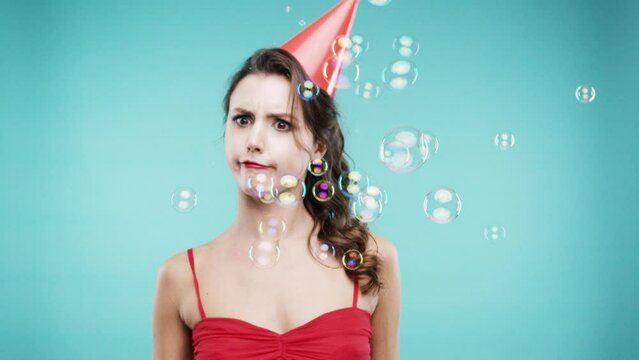 Woman, dance and crazy in studio with bubbles for party, celebration and funny face on new year. Excited young person, winner or model with energy, playful and portrait in hat on a blue background