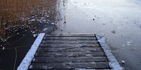 wooden pier and frozen lake with reeds 