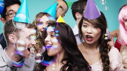 Friends, group and celebration in studio with bubbles for party with props, dancing and happiness. Social event, people and movement with energy, hats and enjoyment at birthday on blue background