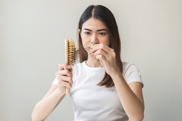 Serious asian young woman holding brush holding comb, hairbrush with fall black hair from scalp...