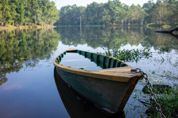 A solitary boat tied to the bank of a tranquil lake in Chitwan National Park, with the calm waters mirroring the lush green backdrop