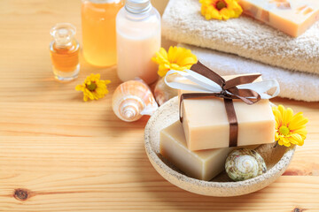 Handmade bars of spa soap collected as a stack. Soft towels and flowers on wooden table, copy space.