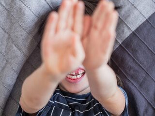 Little boy covers his face with hands. Child refuses to be photographed. Playful kid shows his palm hands instead of laughing face.