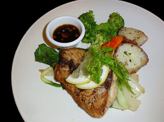 Slice of grilled fish, potatoes and broccoli with soy sauce dip in a white plate.
