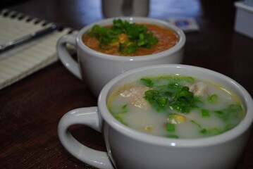 Two cups of different soups with slices of green onions on top.