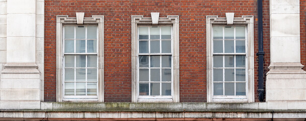 Fototapeta na wymiar three aligned classic white windows of typical London architecture with red brick wall