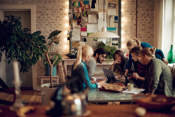 Friends enjoying pizza and looking at laptop together at home