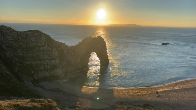 The sun goes down on the Jurassic coast and Durdle Door in Dorset with Seak Pink Trift growing on the top of the cliff in the foreground. Durdle Door, Dorset, Jurassic Coast, England, UK
