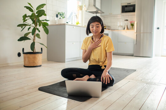 Young adult woman doing yoga with laptop at home